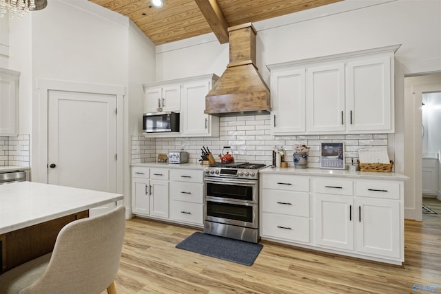 kitchen featuring stainless steel appliances, custom exhaust hood, light countertops, and white cabinets