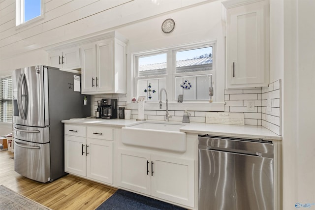 kitchen with a sink, white cabinets, light countertops, appliances with stainless steel finishes, and light wood finished floors