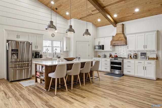 kitchen with white cabinetry, light countertops, appliances with stainless steel finishes, decorative light fixtures, and custom range hood