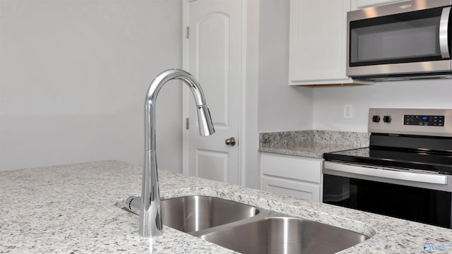 kitchen featuring appliances with stainless steel finishes, white cabinets, and light stone counters