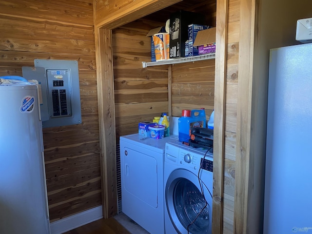 laundry room featuring washer and dryer, electric panel, and wood walls