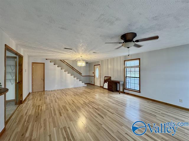 unfurnished living room with ceiling fan with notable chandelier, light hardwood / wood-style floors, and a textured ceiling