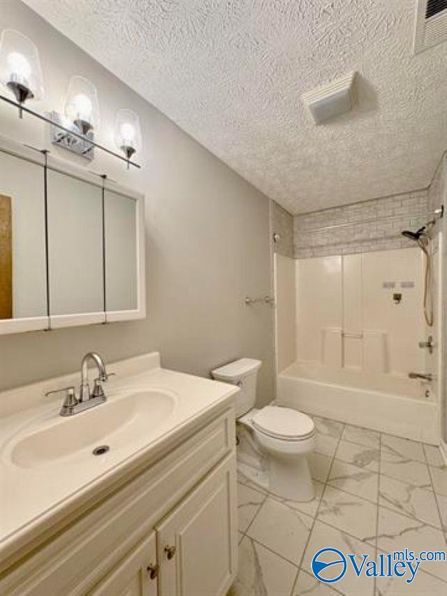 full bathroom with vanity, toilet,  shower combination, and a textured ceiling