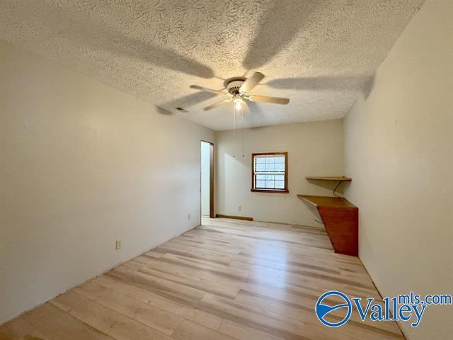 empty room with a textured ceiling, ceiling fan, and light hardwood / wood-style flooring