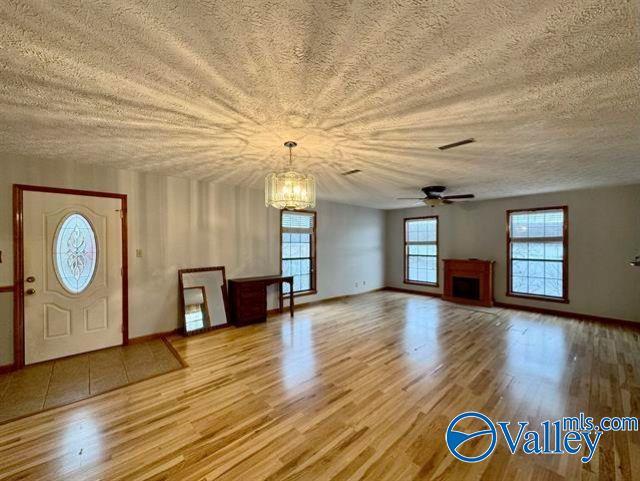 unfurnished living room with ceiling fan with notable chandelier, light hardwood / wood-style floors, and a textured ceiling