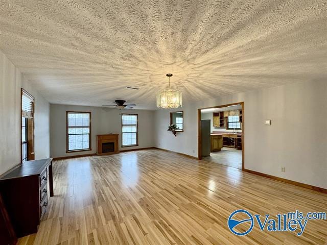 unfurnished living room featuring ceiling fan with notable chandelier, a textured ceiling, and light hardwood / wood-style floors