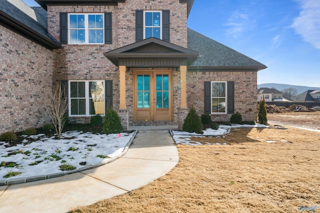 view of exterior entry with french doors, brick siding, and roof with shingles