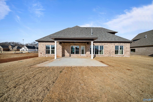 rear view of property with a patio, brick siding, a lawn, and a shingled roof