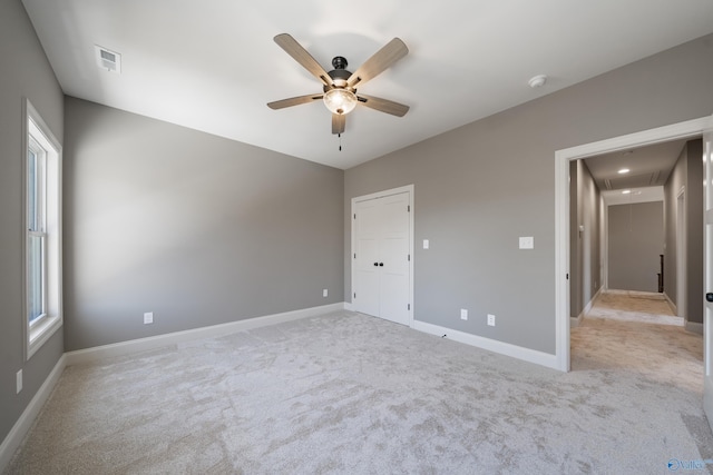 unfurnished room with attic access, visible vents, baseboards, light colored carpet, and ceiling fan