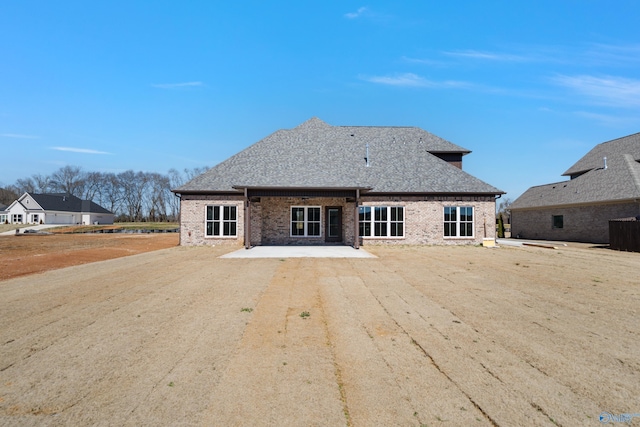 back of property with dirt driveway, brick siding, and roof with shingles