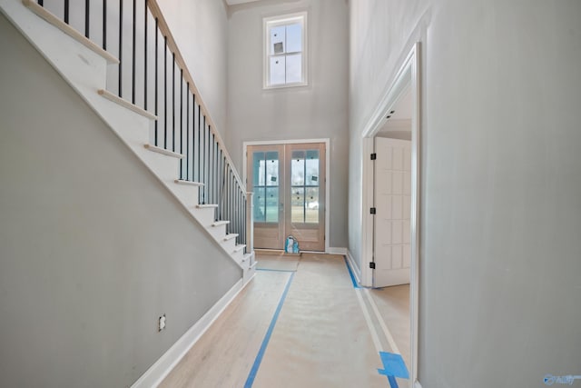 foyer entrance with stairs, a high ceiling, baseboards, and french doors