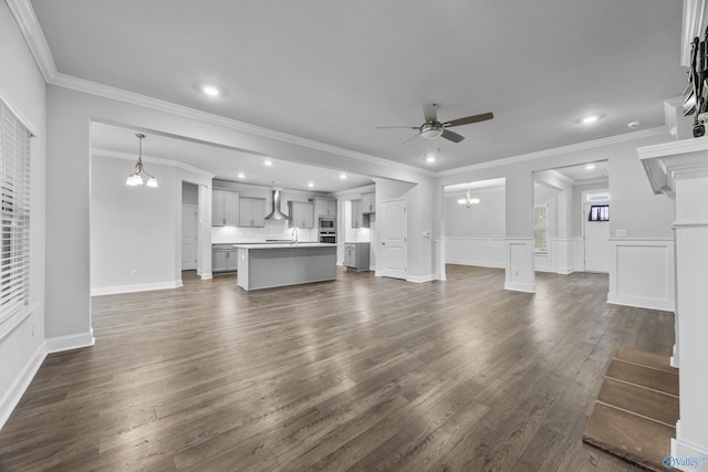 unfurnished living room featuring recessed lighting, dark wood finished floors, ornamental molding, and ceiling fan with notable chandelier