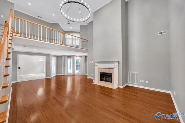 114 Canterbury Dr, Madison, AL 35758 - unfurnished living room with a chandelier, a towering ceiling, stairs, a tiled fireplace, and wood finished floors