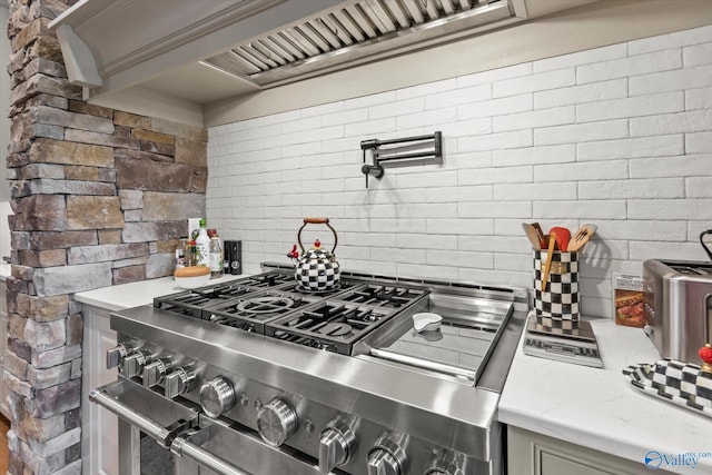 kitchen with backsplash, gray cabinets, light stone countertops, and high end stainless steel range