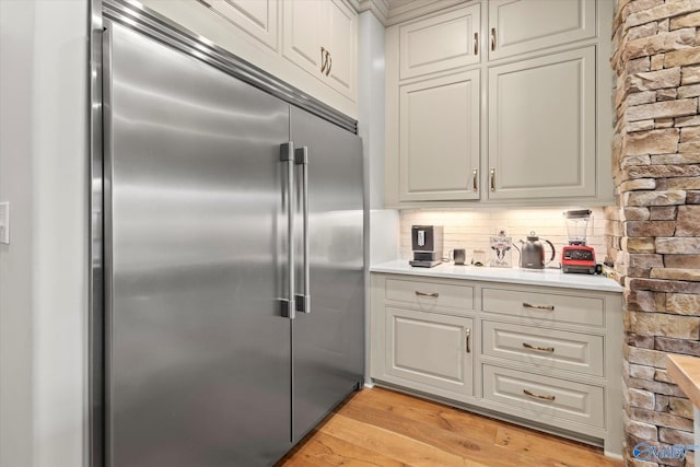 kitchen with stainless steel built in refrigerator, light wood-type flooring, and backsplash