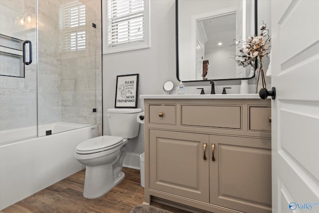 full bathroom featuring ornamental molding, bath / shower combo with glass door, vanity, hardwood / wood-style flooring, and toilet