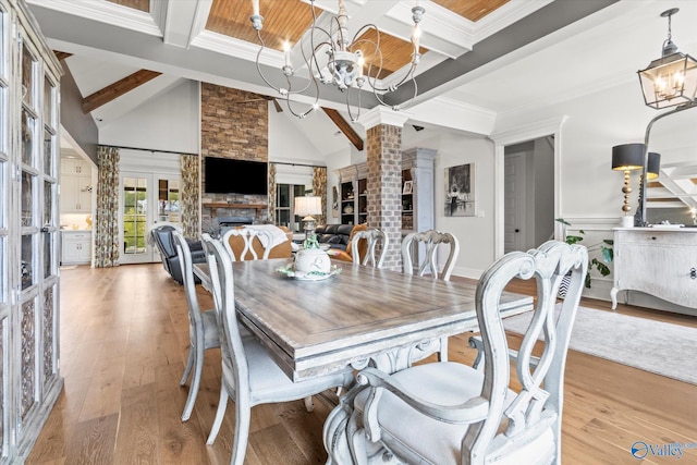 dining area with decorative columns, light hardwood / wood-style flooring, beamed ceiling, a chandelier, and a stone fireplace