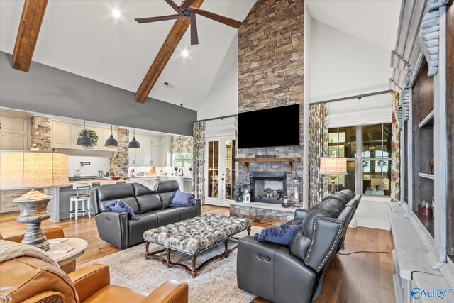 living room featuring ceiling fan, light hardwood / wood-style floors, a stone fireplace, and high vaulted ceiling