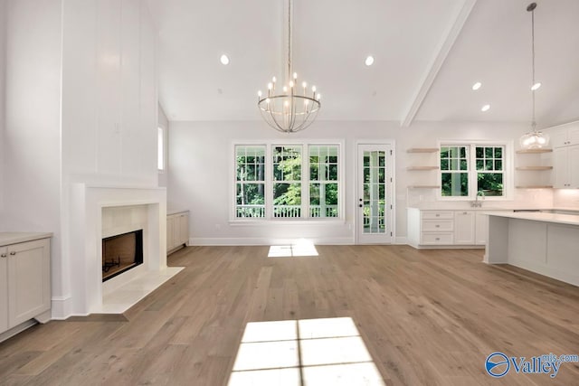 unfurnished living room with sink, vaulted ceiling with beams, a notable chandelier, a high end fireplace, and light hardwood / wood-style floors