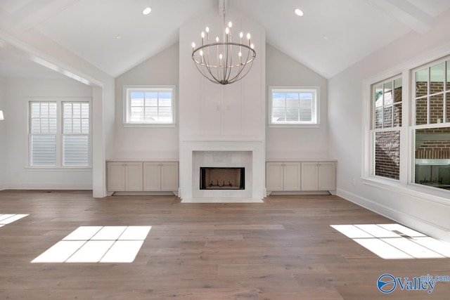 unfurnished living room with lofted ceiling with beams, a large fireplace, a notable chandelier, and light hardwood / wood-style floors