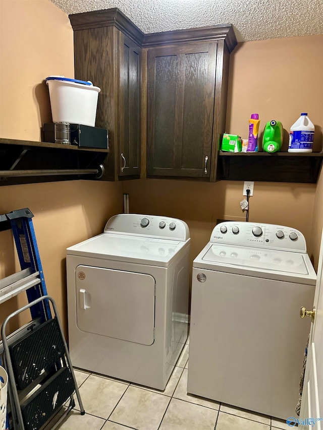 laundry room featuring cabinets, light tile patterned flooring, washing machine and dryer, and a textured ceiling