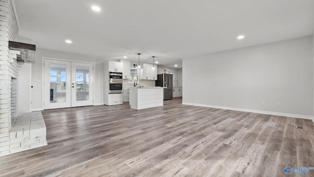 unfurnished living room featuring a fireplace, french doors, sink, and light hardwood / wood-style flooring