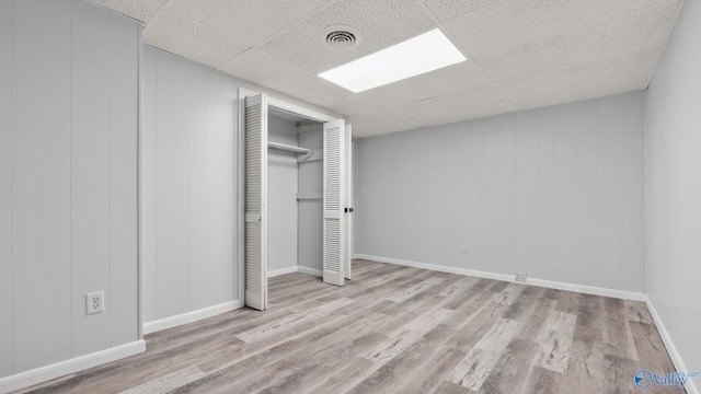 unfurnished bedroom featuring a drop ceiling, a closet, and light hardwood / wood-style flooring