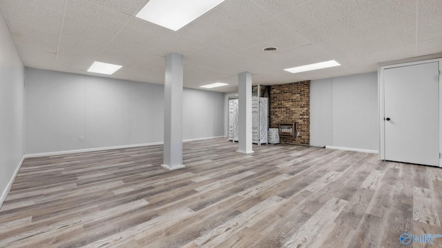 basement with a drop ceiling, light hardwood / wood-style floors, and a fireplace