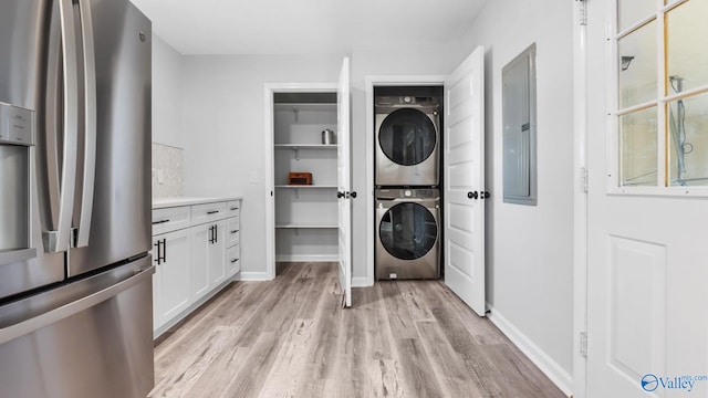 laundry area with electric panel, stacked washer and clothes dryer, and light wood-type flooring