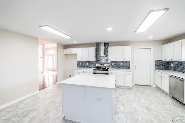 kitchen with appliances with stainless steel finishes, backsplash, wall chimney range hood, white cabinets, and a center island