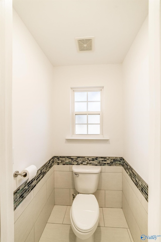 bathroom with toilet, tile patterned floors, and tile walls