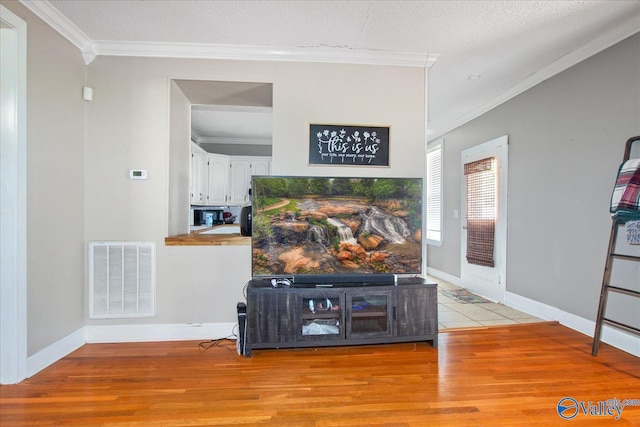 living area with light wood-style floors, a textured ceiling, visible vents, and crown molding