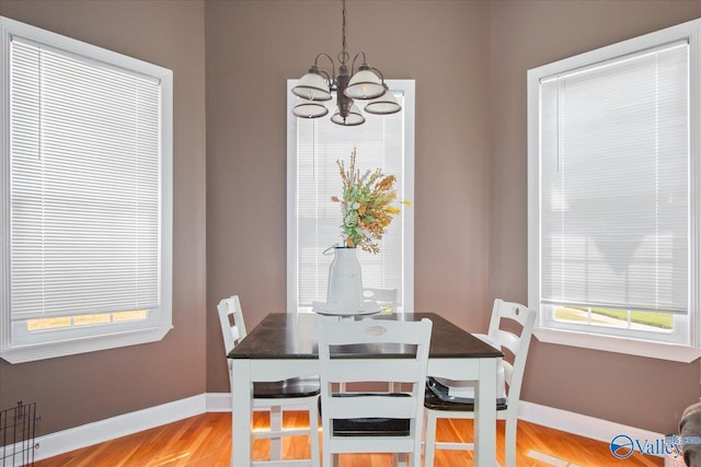 dining area featuring light wood-style floors, a healthy amount of sunlight, baseboards, and an inviting chandelier