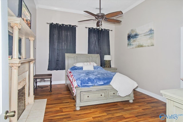 bedroom featuring a fireplace, crown molding, baseboards, and wood finished floors