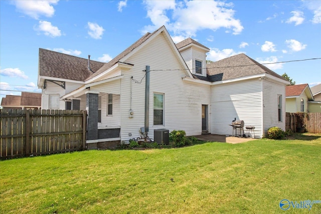 rear view of property featuring a yard, central AC unit, roof with shingles, and fence