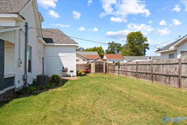 view of yard featuring an outbuilding, a fenced backyard, a storage shed, and central AC unit