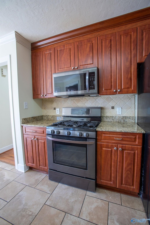 kitchen with stainless steel appliances, tasteful backsplash, light stone countertops, and a textured ceiling