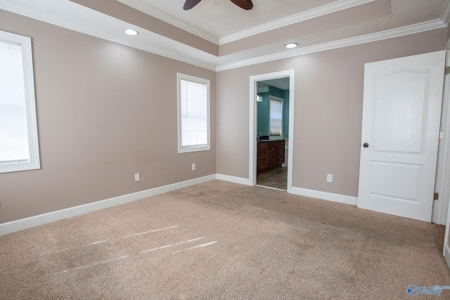 unfurnished bedroom with ensuite bath, ornamental molding, a raised ceiling, and carpet