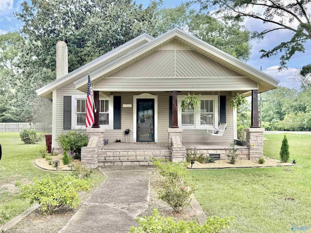 view of front of house featuring covered porch, a front lawn, and a chimney