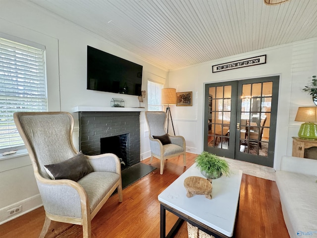 sitting room featuring a brick fireplace, french doors, crown molding, and wood finished floors