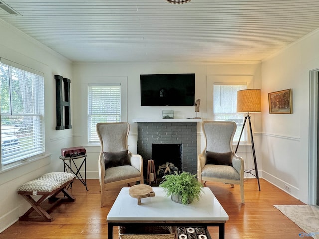 living area with a brick fireplace, visible vents, crown molding, and light wood-style flooring