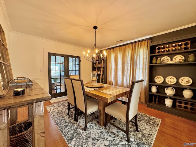 dining area with visible vents, ornamental molding, wood finished floors, french doors, and a chandelier