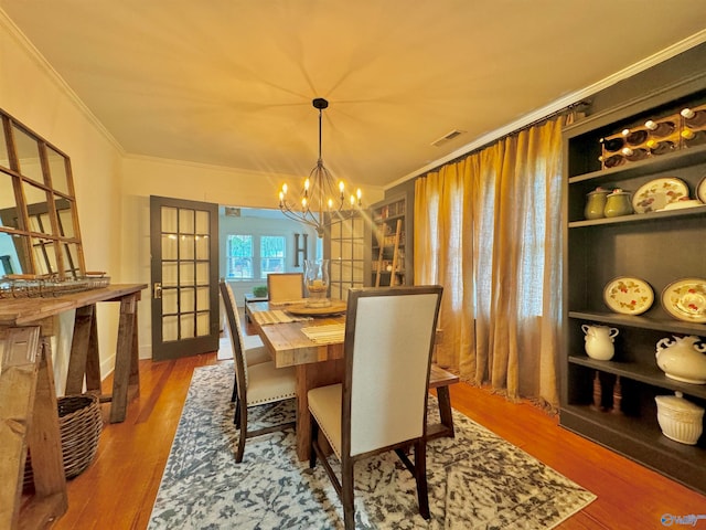 dining space featuring ornamental molding, an inviting chandelier, wood-type flooring, and french doors