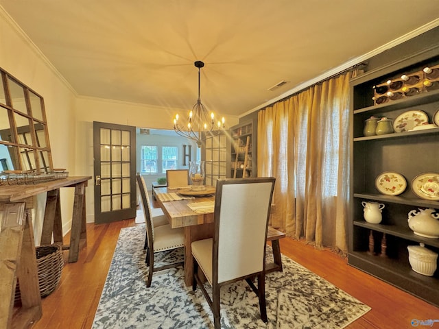 dining area with a notable chandelier, crown molding, and wood finished floors