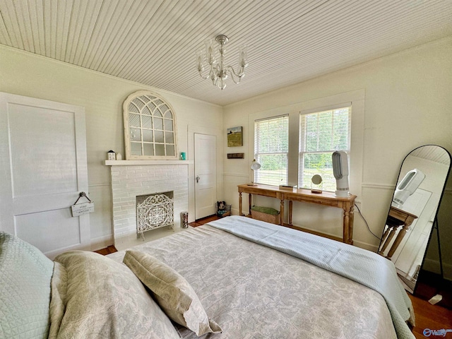 bedroom with wood-type flooring, a notable chandelier, and a brick fireplace