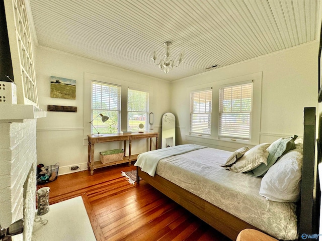 bedroom with a stone fireplace, wood-type flooring, and an inviting chandelier