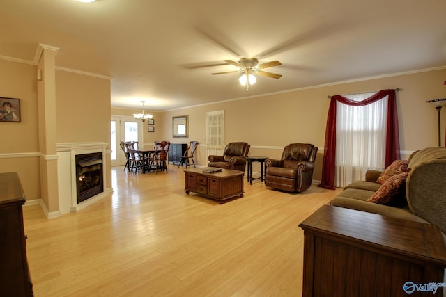 living area featuring light wood-style floors, a fireplace, ornamental molding, and ceiling fan with notable chandelier