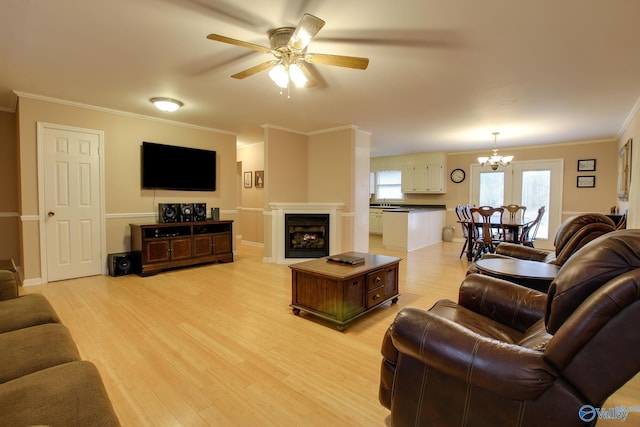 living room featuring light wood finished floors, a fireplace, ornamental molding, and ceiling fan with notable chandelier