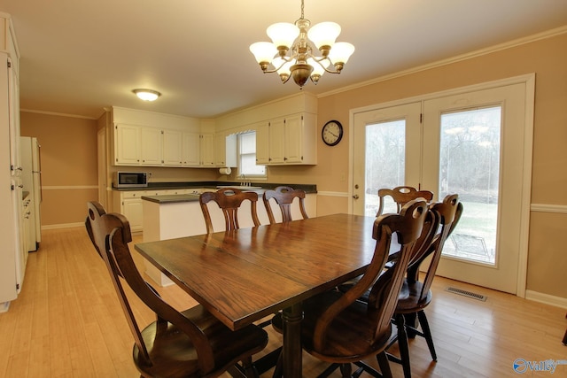 dining room featuring crown molding, visible vents, a chandelier, light wood-type flooring, and baseboards