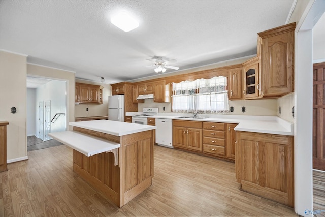 kitchen featuring glass insert cabinets, white appliances, light countertops, and brown cabinets